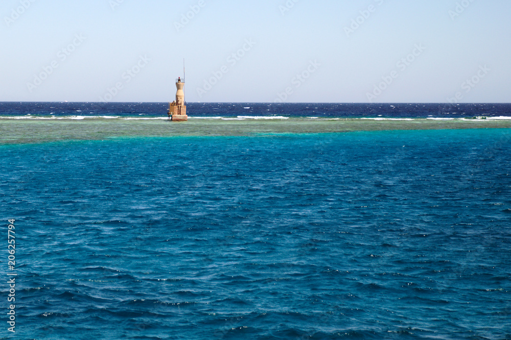 Seascape with a remote lighthouse. One lighthouse against the backdrop of a calm sea surface and blue sky