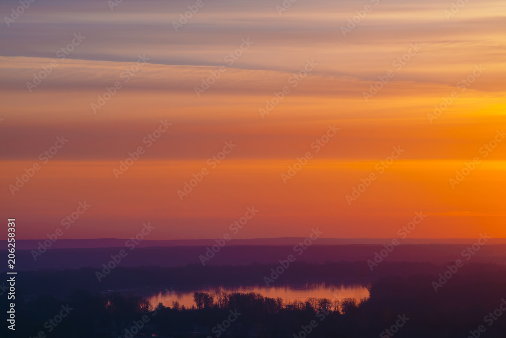 River under varicolored striped warm sky. Horizontal lines of picturesque clouds. Atmospheric background image of lake with reflection of dawn sky.
