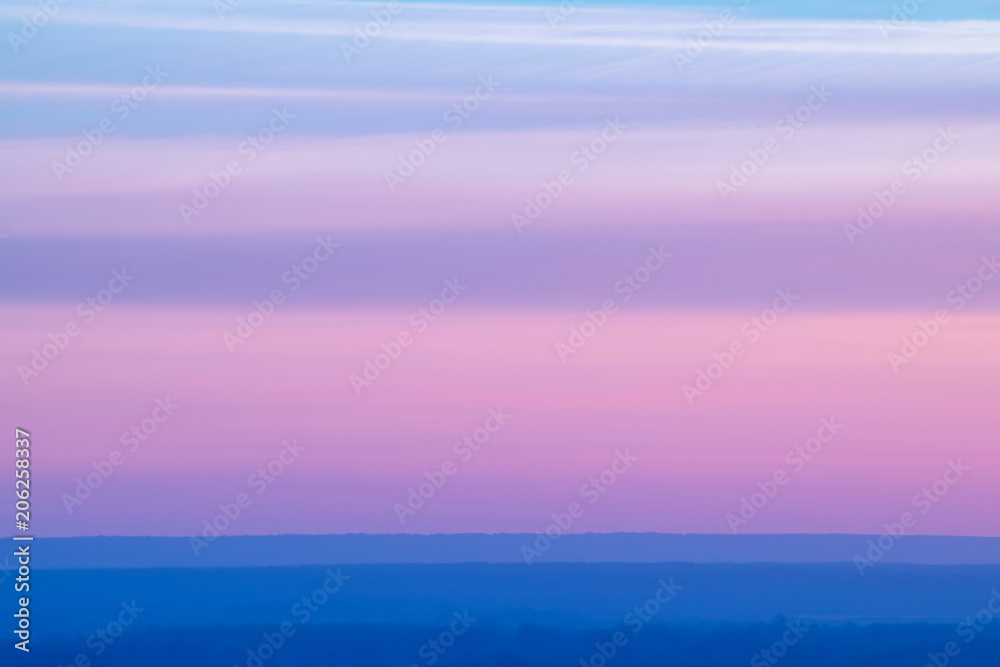 Varicolored striped surreal sky with shades of blue, cyan, pink, purple, magenta colors with cobalt land. Horizontal lines of smooth clouds. Atmospheric background image of tender sky.