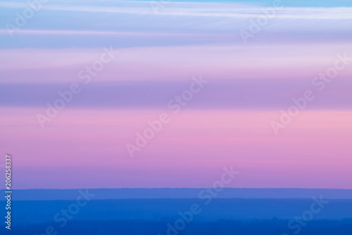 Varicolored striped surreal sky with shades of blue, cyan, pink, purple, magenta colors with cobalt land. Horizontal lines of smooth clouds. Atmospheric background image of tender sky.