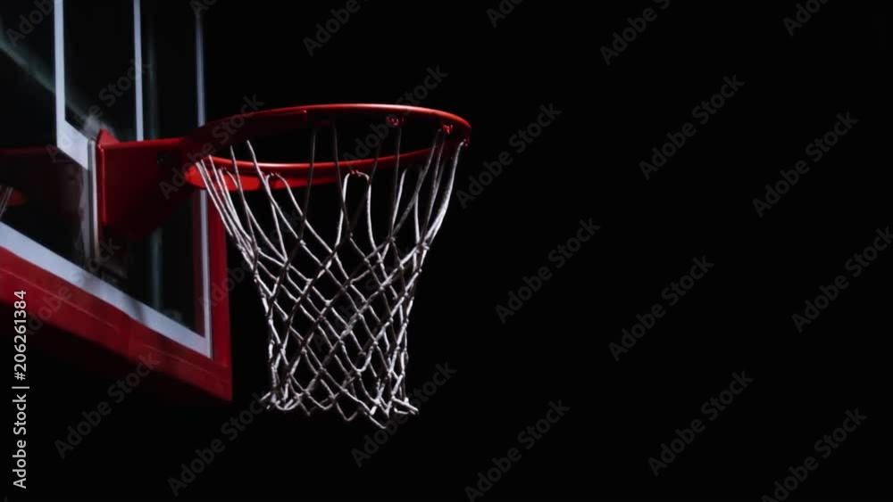 Close up of a slam dunk on a basketball hoop on a darkly lit court Close up of a slam dunk on a basketball hoop on a darkly lit court