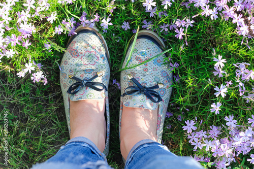 Feet of a girl in fashionable ragged jeans and shoes. Around the flowers. Spring. Summer. Concept. View from above.