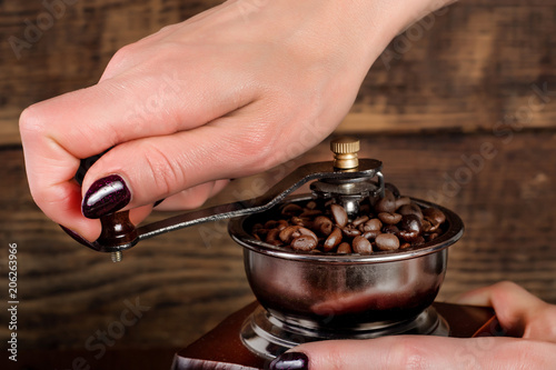Woman hand grinding coffee roasted beans in retro mill and wooden background. Retro and Vintage concept drink and food. Close up, selective focus