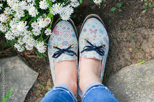 Feet of a girl in fashionable ragged jeans and shoes. Around the flowers. Spring. Summer. Concept. View from above.
