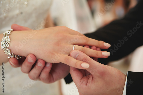 The groom puts a white gold engagement ring on his finger