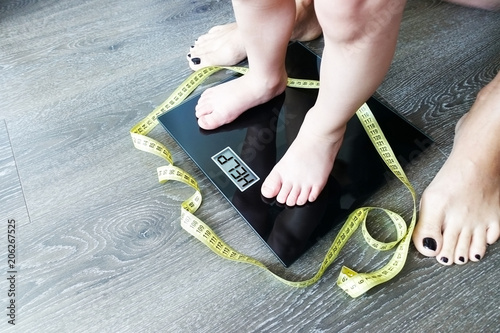 Help fat or obese child with toddler on weight scale, supervised by a parent
