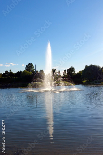 fountain on lake reflected in water, against blue sky background © zakob