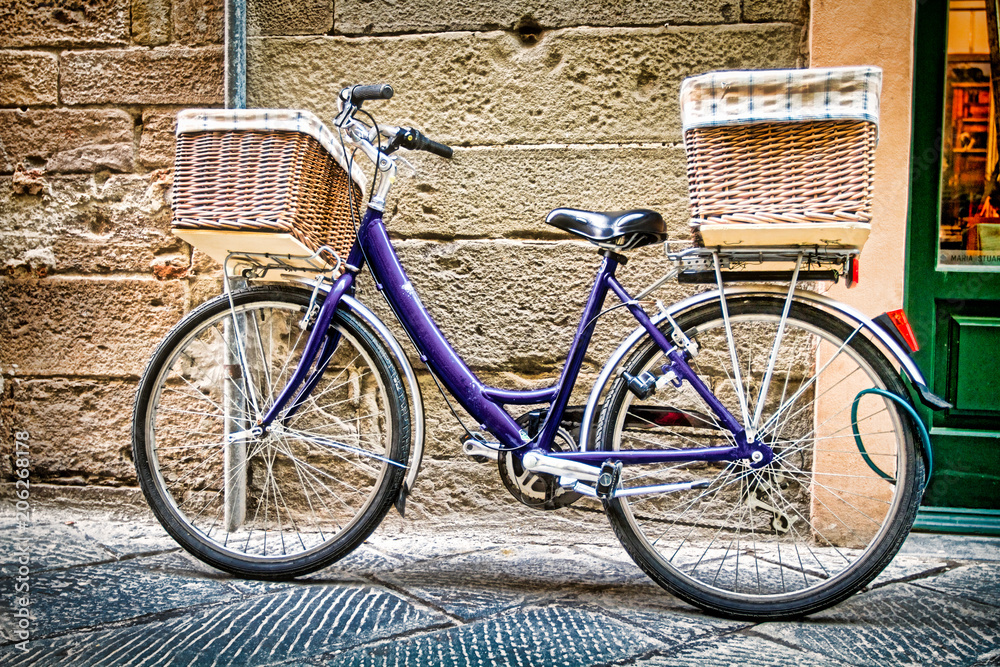 Blue bicycle with woven baskets leans against a stone wall