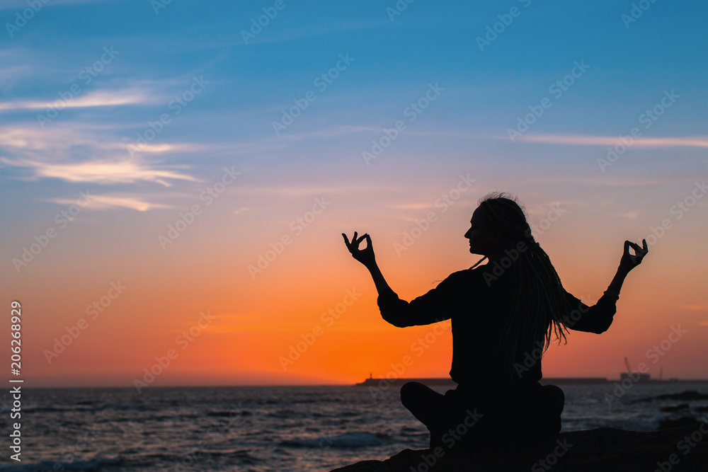 Silhouette of yoga woman meditation on the ocean during amazing sunset.