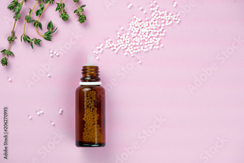 Flat lay of brown glass bottle with plenty of white homeopathic pills on pink surface. Homeopathic lactose sugar balls in glass bottles,medicine. Bottle with white sugar pills photo