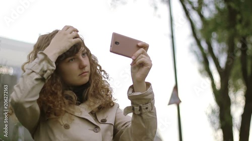 Pretty woman arranging her hair on the street with the help of a Smartphone.