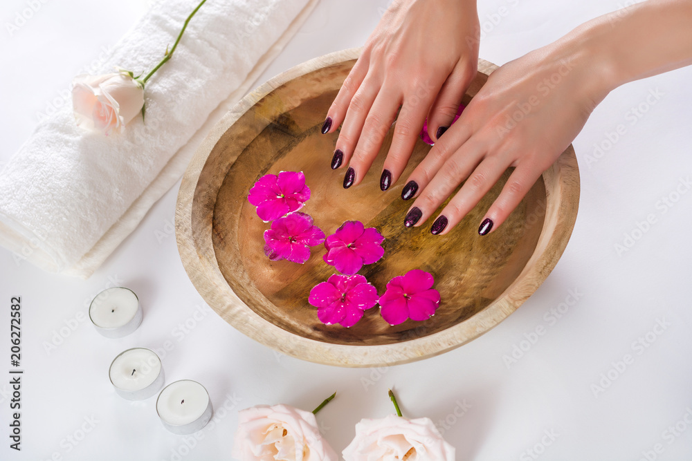 Female hands with manicured fashion nails with purple varnish in a wooden bowl with water and purple flower. Spa beauty treatment concept. Close up, selective focus Female hands with manicured fashion nails with purple varnish in a wooden bowl with water and purple flower. Spa beauty treatment concept. Close up, selective focus