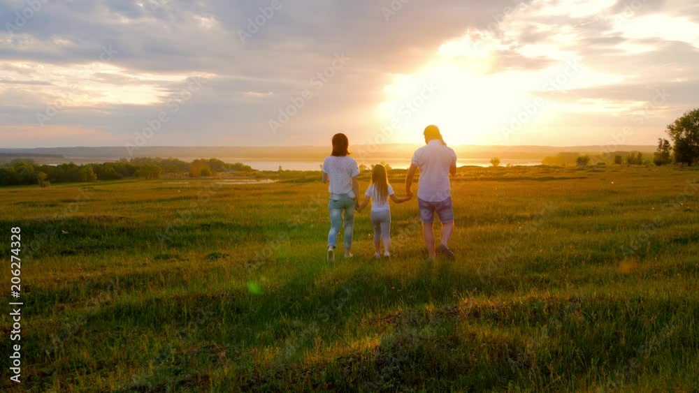 A family with children is walking along the green meadow towards the sunset. Run, raising baby up in the air, hugs, love, playing. We are happy family. A family with children is walking along the green meadow towards the sunset. Run, raising baby up in the air, hugs, love, playing. We are happy family.