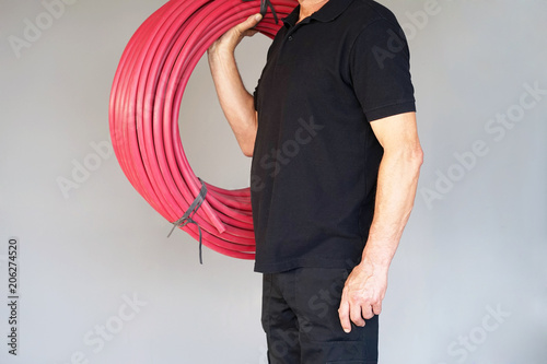 The electrician holds red a roll of an electric protective tube on a gray background. The concept of industrial and private services.