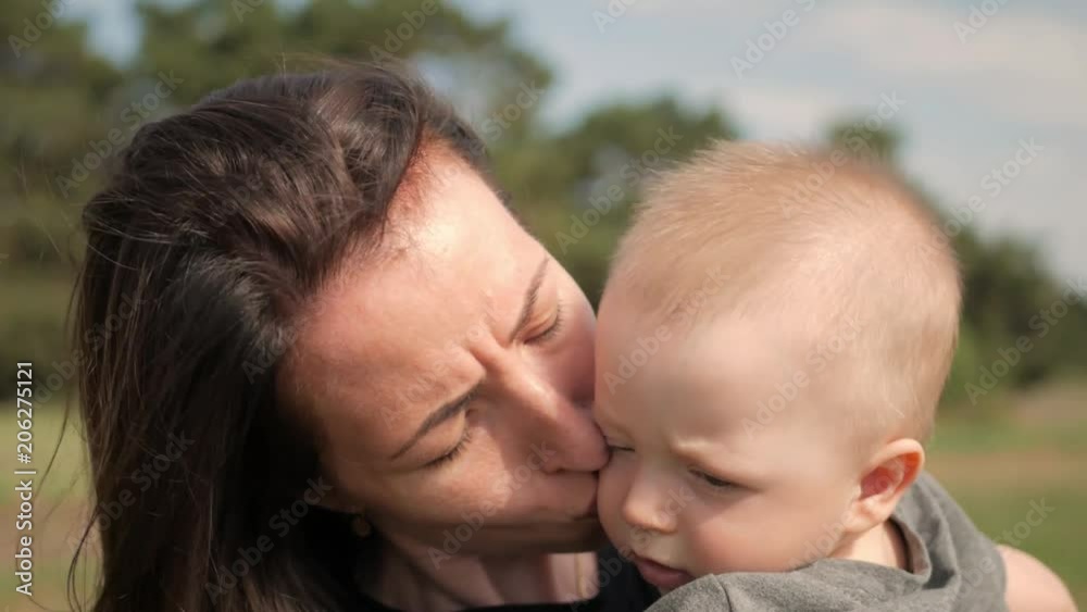 Happy family on nature outdoors mother kissing little baby boy on the green meadow. Happy family on nature outdoors mother kissing little baby boy on the green meadow.