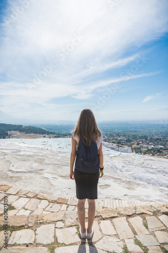 An unknown girl stands with her back standing on a rock looking at the landscape of mountains under a blue sky with light cirrus clouds on a bright sunny day. Denizli. Pamukale. Turkey photo