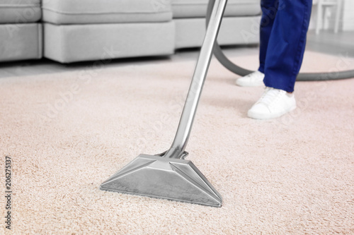 Male worker removing dirt from carpet with professional vacuum cleaner indoors photo