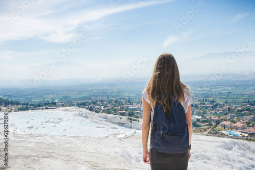 An unknown girl stands with her back standing on a rock looking at the landscape of mountains under a blue sky with light cirrus clouds on a bright sunny day. Denizli. Pamukale. Turkey photo