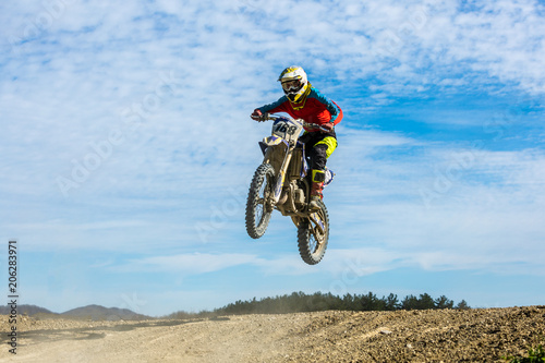 racer on a motorcycle in flight  jumps and takes off on a springboard against the sky.