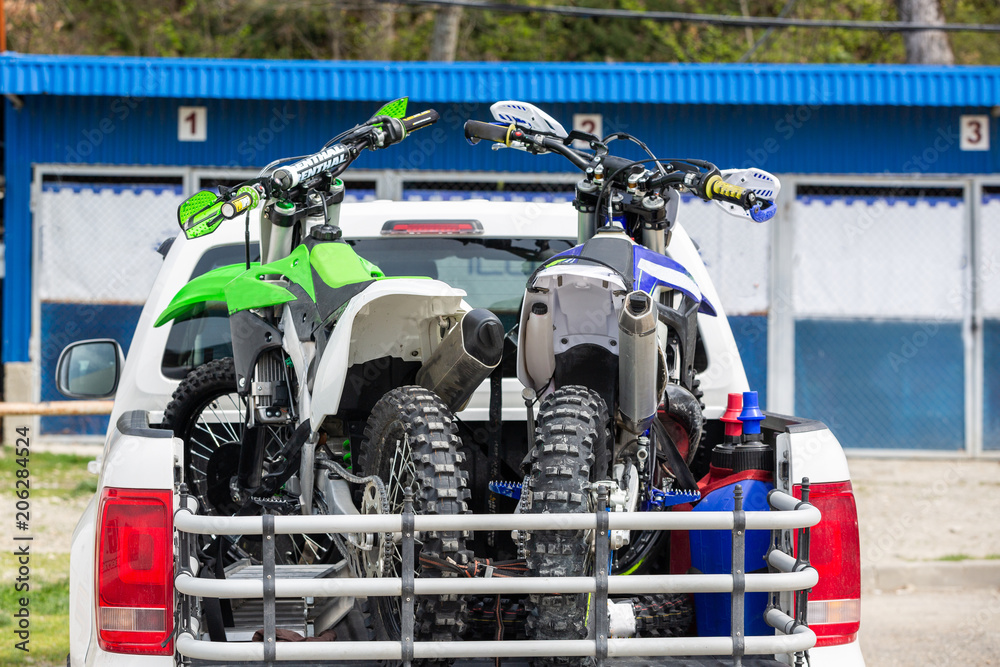 Fototapeta premium Rear viwe with two dirt bike motorcycles on the back of the truck with safety gear in residential setting.