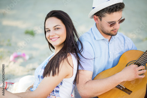 Young couple sitting on the beach and playing guitar