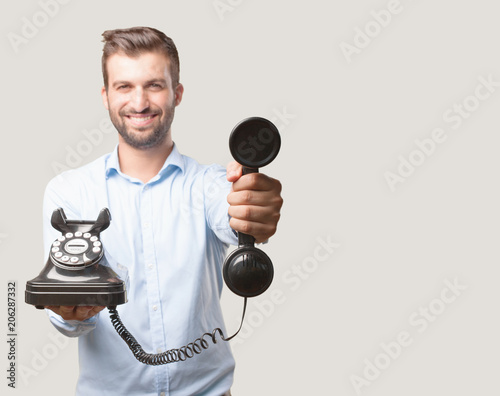 young happy and handsome man, blue t shirt, smiling holding a vintage black telephone . person isolated against monochrome background photo