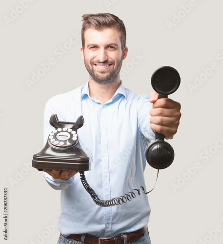 young happy and handsome man, blue t shirt, smiling holding a vintage black telephone . person isolated against monochrome background photo