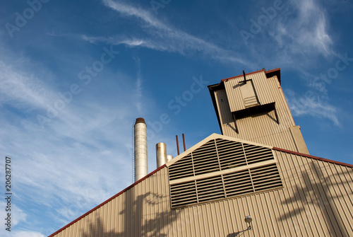 Factory building and chimney with a cloud like smoke early in the morning against a dramatic blue sky