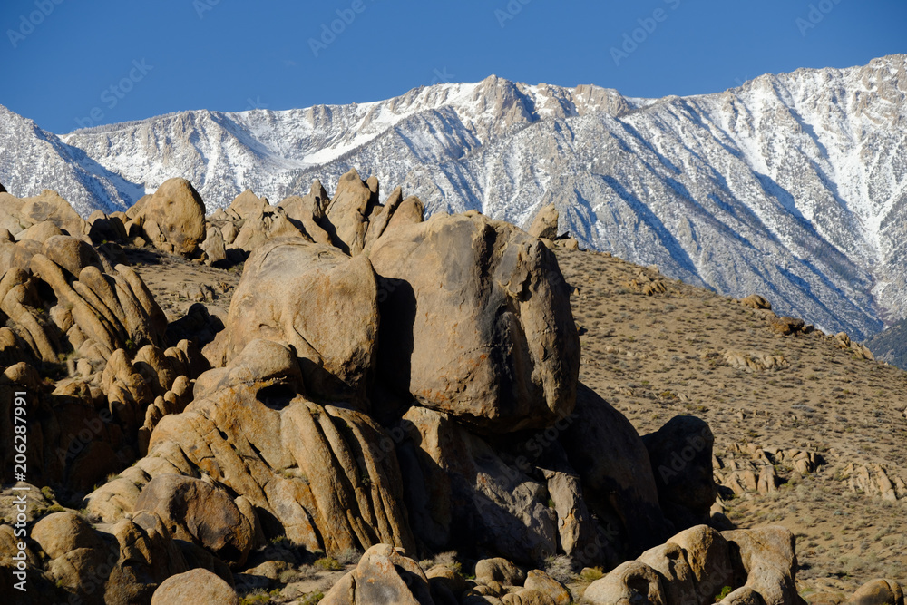 The Rugged and carved granite boulders of Alabama Hills in the desert near the snow-covered tall peaks of the Eastern Sierra Mountains and Mt Whitney Eastern California