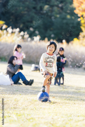 逆光がさす秋の公園でボール遊びをする5歳の男の子