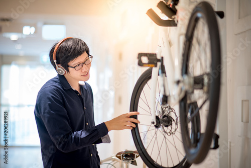 Young Asian man with headphones and glasses looking for bicycle at bike shop in department store, urban lifestyle in shopping mall concept