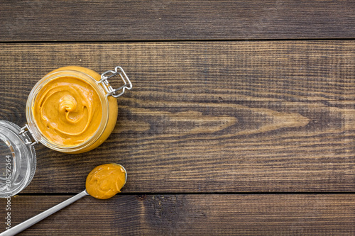 Nut butter in glass jar and spoon with butter on dark wooden background top view copy space