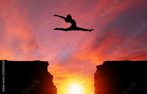 Silhouette of Girl Leaping Over Cliffs With Sunset Landscape