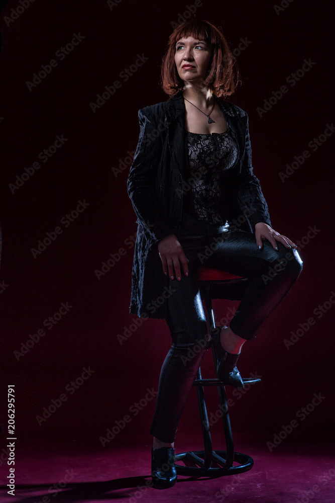 Confident ugly woman wearing black suit siting and posing in front of camera on stage with crimson floor
