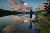 Man standing next to a tranquil lake with an amazing mountain reflection.