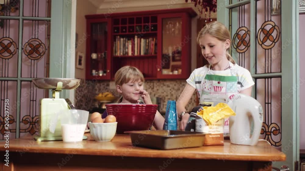 Slider shot of two sisters checking the cookbook before adding the ingredients to bake a cake in the kitchen.
