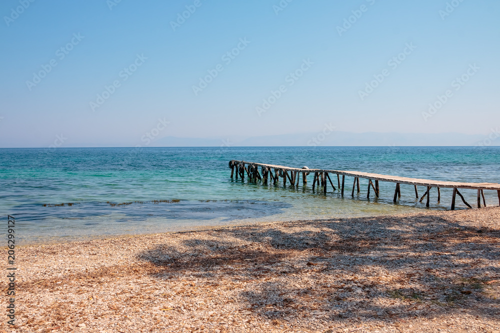Wooden pier turquoise sea water sunny day, stones beach, greece island. Romantic wild place. Clear water sea. wooden pier goes to the sea, Sunny weather, the horizon line.Copy space