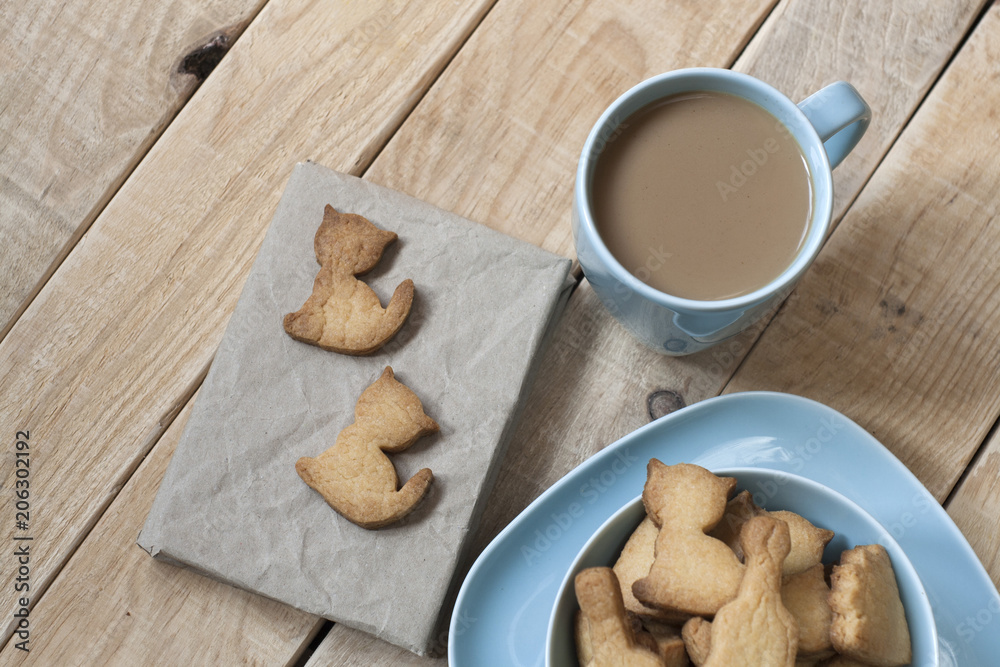 Delicious gingerbread cookies on a blue plate, a cup of coffee with milk and a craft notebook. Delicious gingerbread cookies on a blue plate, a cup of coffee with milk and a craft notebook.