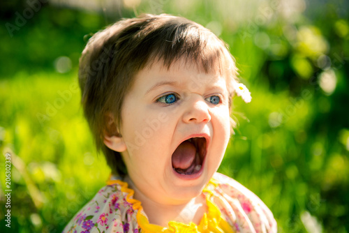 Little girl with open mouth. Funny expressive girl in the park. Children's whims. 