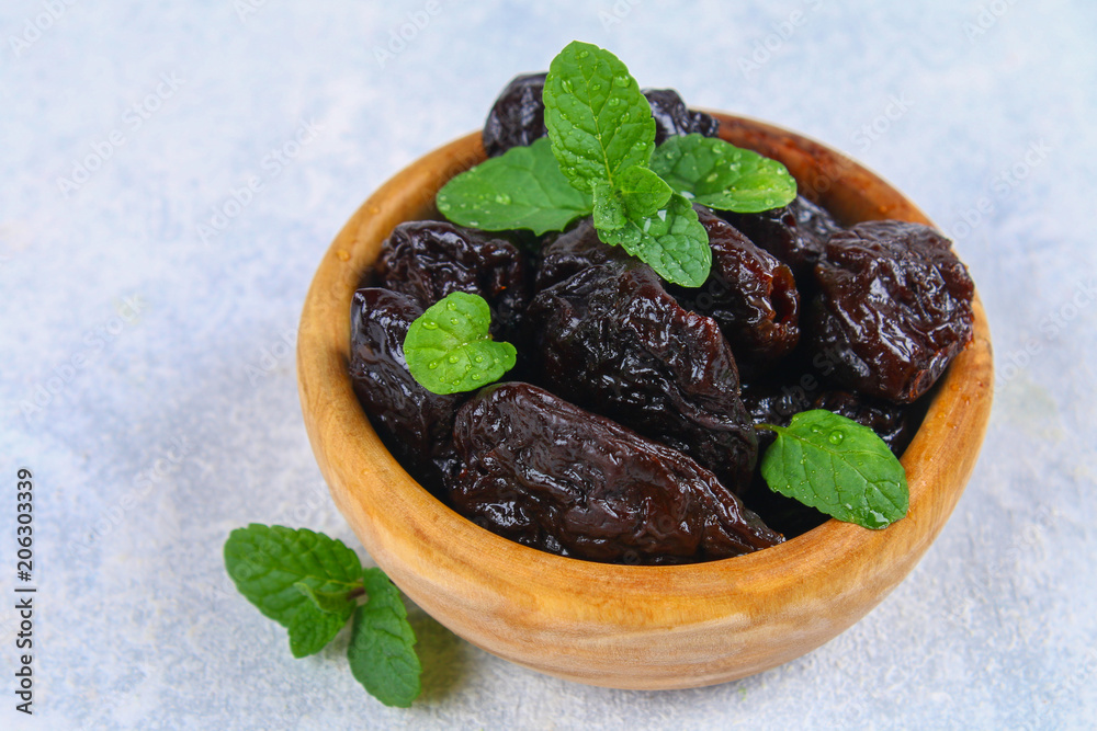 Prunes and fresh mint leaves in a bowl on a concrete table. Prunes and fresh mint leaves in a bowl on a concrete table.