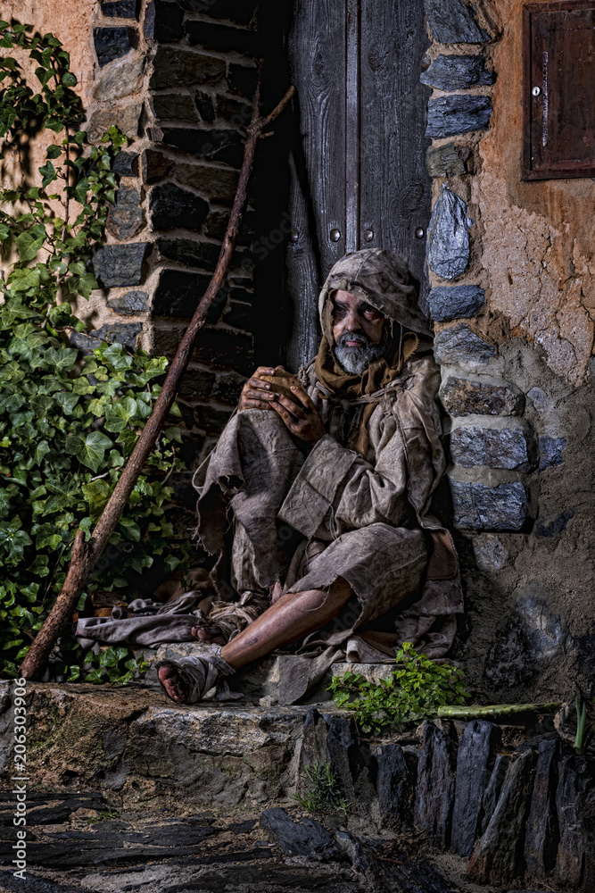 Man, dressed in rags, begging through the streets of a village Man, dressed in rags, begging through the streets of a village