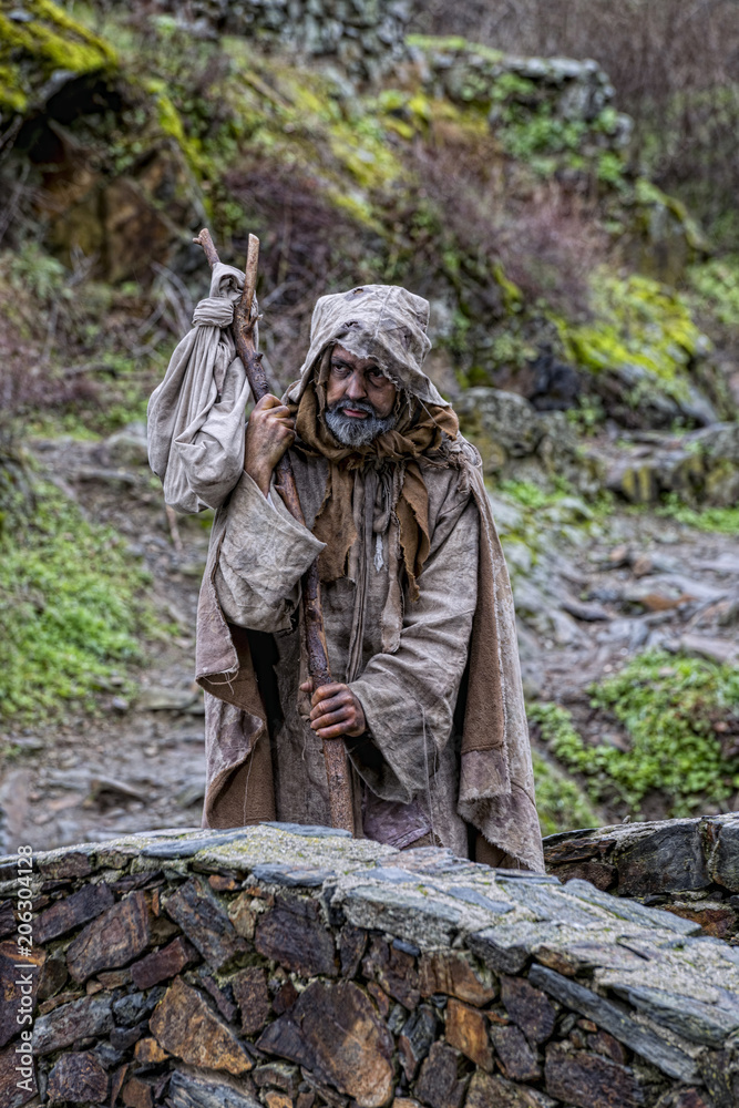 Man, dressed in rags, begging through the streets of a village