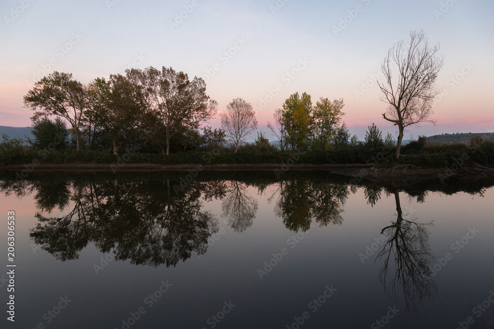 A symmetric photo of a lake, with trees and clouds reflections o