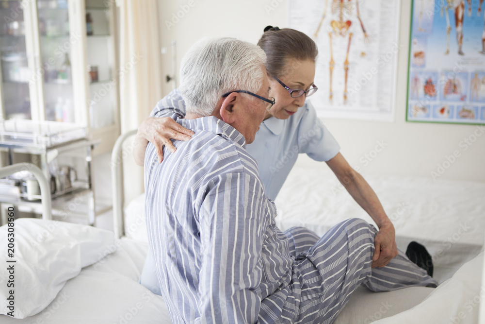 © Monet - 足を怪我している患者。介護士がベッドに寝かせる手伝いをしている。