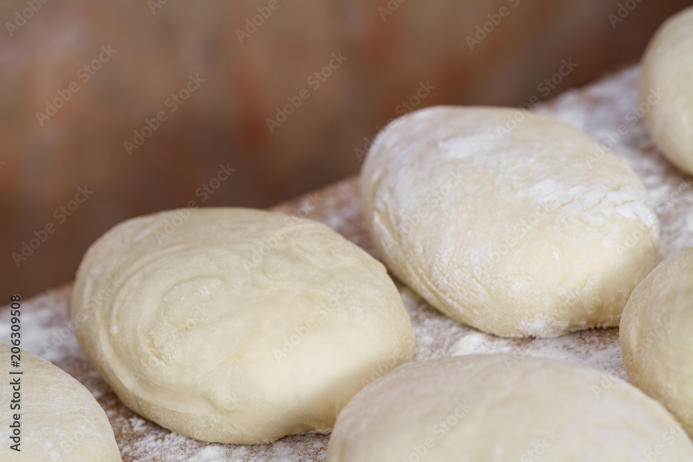 Raw homemade pies. Uncooked patties from yeast dough with stuffing are lying on a wooden plank and ready for baking. Closeup, selective focus, brick background Raw homemade pies. Uncooked patties from yeast dough with stuffing are lying on a wooden plank and ready for baking. Closeup, selective focus, brick background