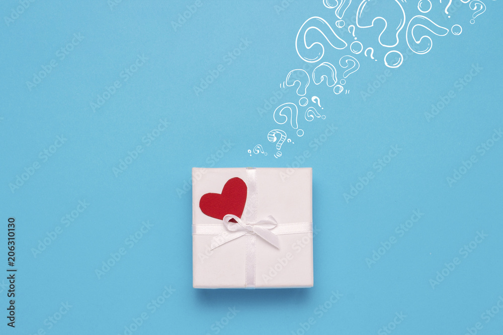 White gift box, red heart and Icon Question mark on a blue background. Minimalistic style. Concept surprise and suspense, a gift from a loved one. Flat lay, top view White gift box, red heart and Icon Question mark on a blue background. Minimalistic style. Concept surprise and suspense, a gift from a loved one. Flat lay, top view
