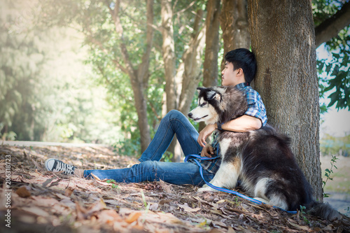 Young man sitting under a tree with a Siberian Husky dog. photo