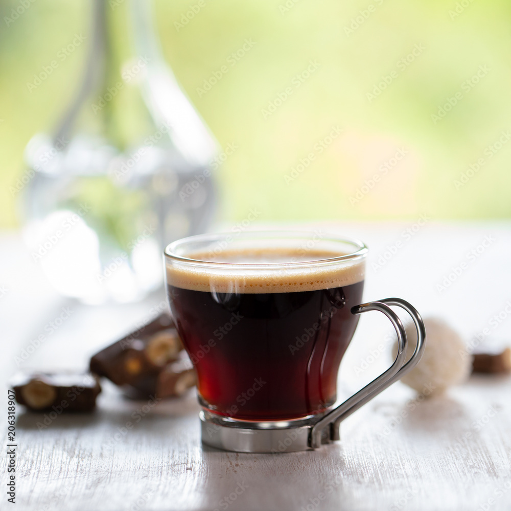 a cup of coffee with chocolate on white wooden table with green leaves background a cup of coffee with chocolate on white wooden table with green leaves background