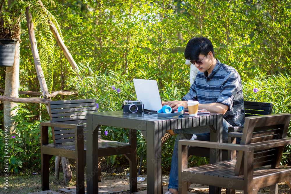 Fototapeta premium Young man wearing glasses sitting using a laptop in a garden