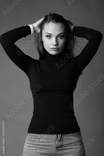 Young, stylish, beautiful girl in dark clothes on a gray background